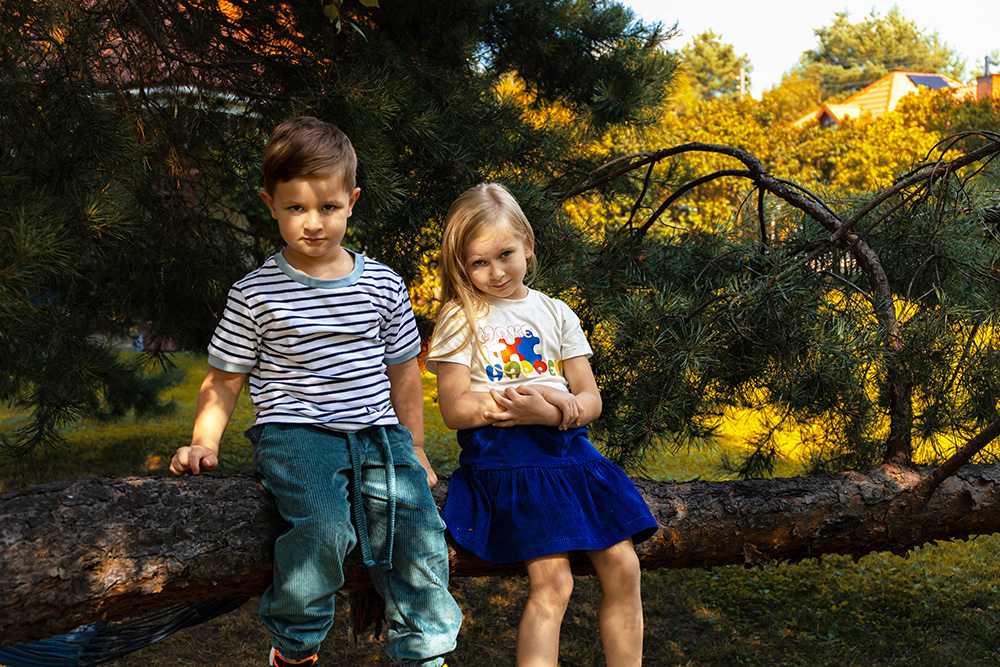 Dzieci siedzące na konarze w ubraniach marki Facile Cotton